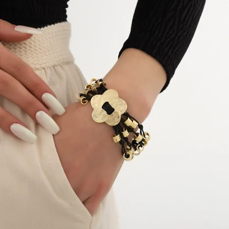 Bracelet noir et doré avec une fleur et des perles, porté sur un poignet.